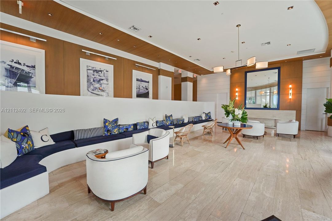 Expansive lobby featuring polished stone flooring, wood-paneled walls, a custom curved built-in seating structure, recessed ceiling lighting, and a modern tiered chandelier