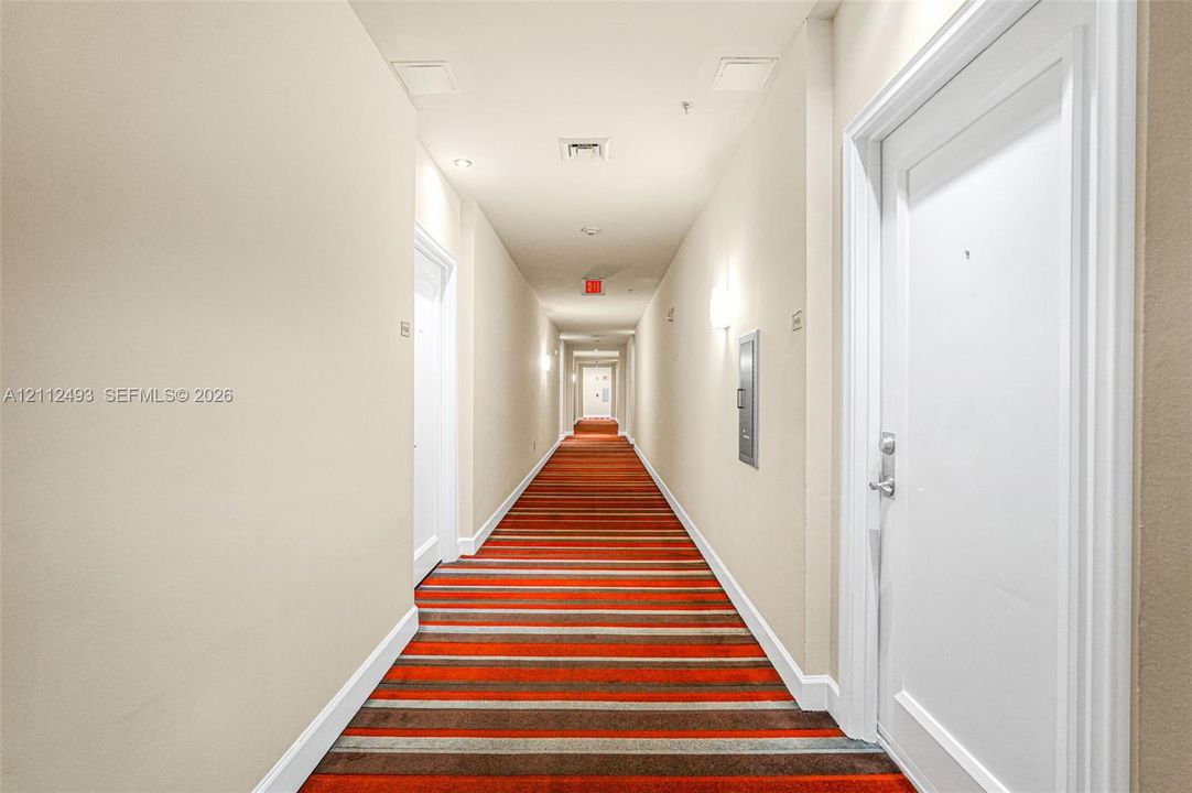 Interior hallway featuring striped carpeting, solid-core doors, and wall-mounted sconce lighting