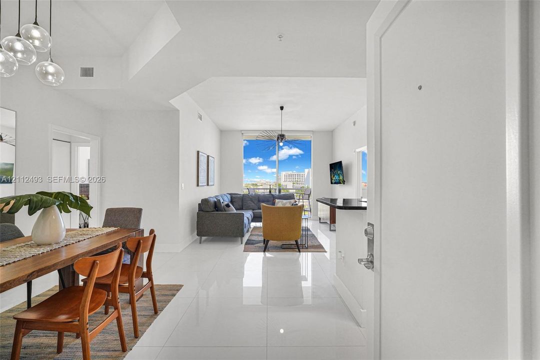 Open-concept living space featuring high-gloss tile flooring, floor-to-ceiling windows, modern multi-pendant lighting, and a breakfast bar with stone-finish countertop