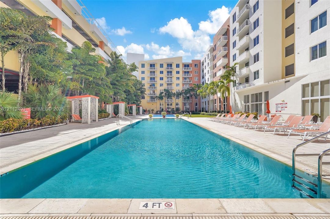 Lap pool featuring a stone-paver deck, built-in covered cabanas, and mature palm landscaping