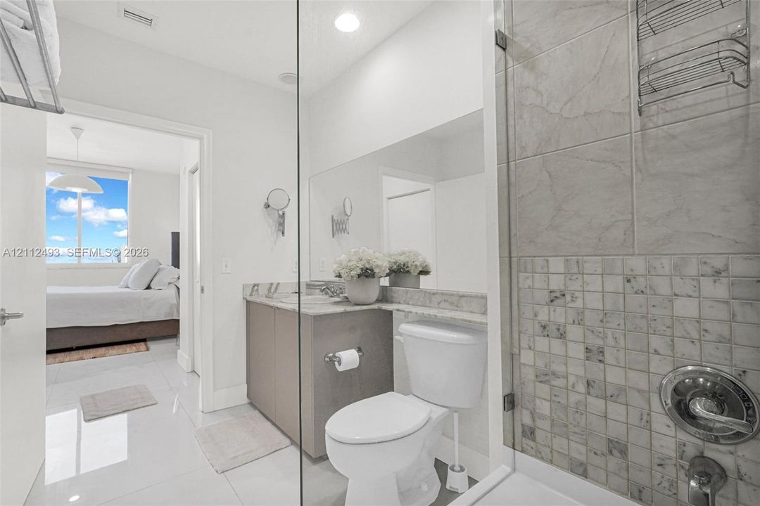 Bathroom featuring polished tile flooring, vanity with stone-finish countertop, full-width mirror, and shower enclosure with decorative stone-tile inlay
