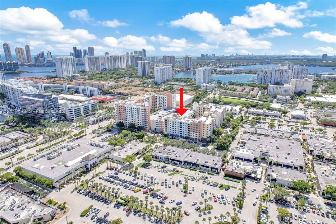 Aerial perspective of a multi-story residential building located within a high-density urban district, featuring proximity to major retail centers and waterfront surroundings