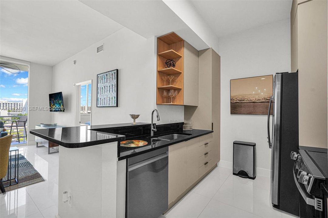 Kitchen featuring high-gloss cabinetry, a black stone countertop breakfast bar, built-in open shelving, stainless steel appliances, and tile flooring