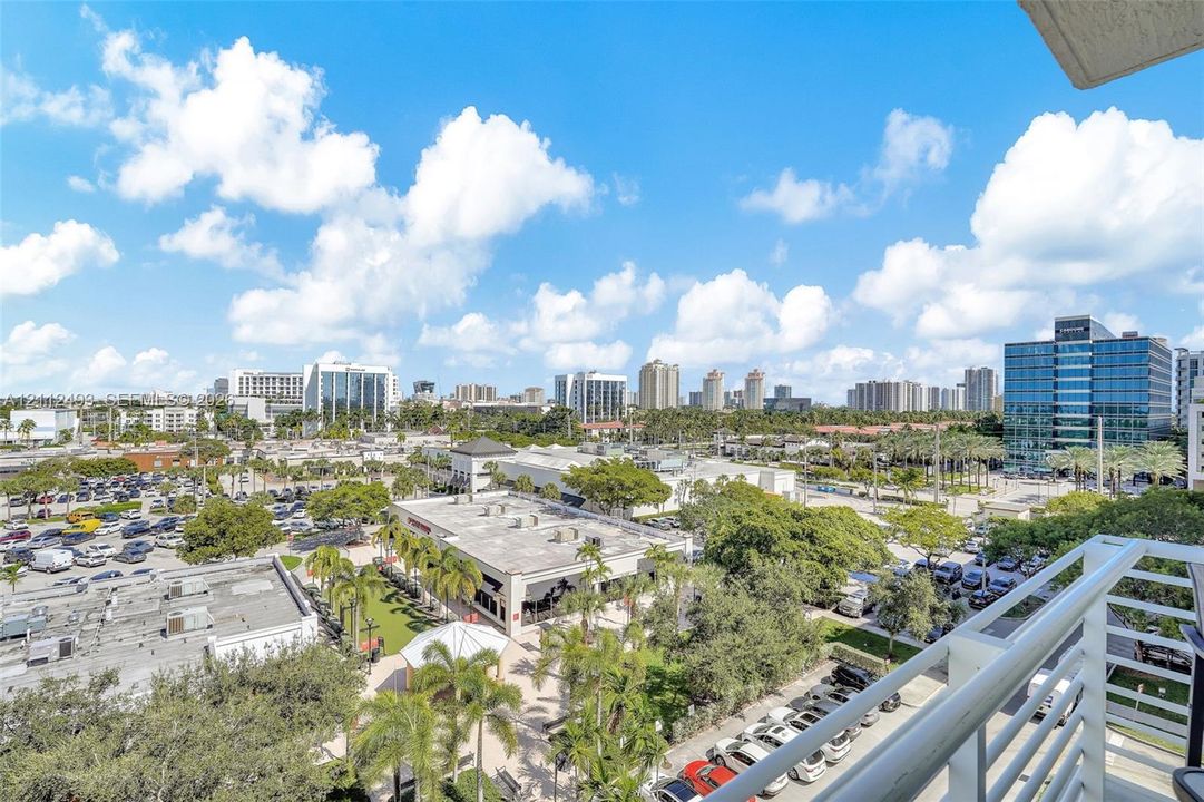 Elevated balcony featuring a white metal railing overlooking a cityscape with palm trees
