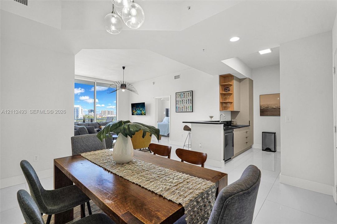 Open-concept interior featuring polished tile flooring, tray ceilings with multi-bulb pendant lighting, and floor-to-ceiling windows