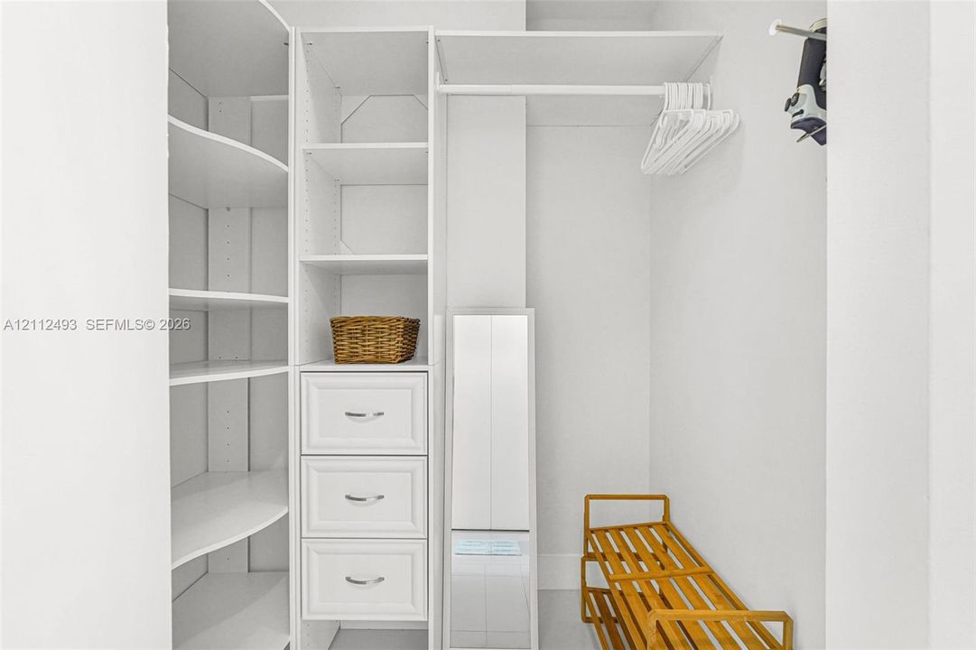 Custom walk-in closet featuring white built-in shelving, a tiered drawer unit with metallic pulls, and an integrated hanging rod