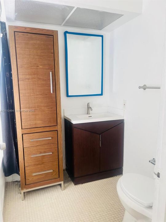 Bathroom featuring a dark wood-finish vanity with an integrated basin, a tall matching wood-finish storage cabinet, and a wall-mounted mirror