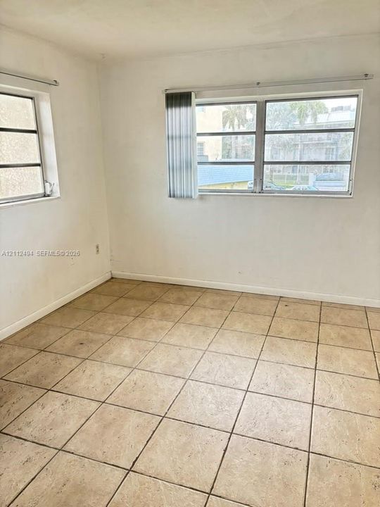 Room featuring light-toned tile flooring, neutral wall finishes, and multiple windows with installed vertical blinds