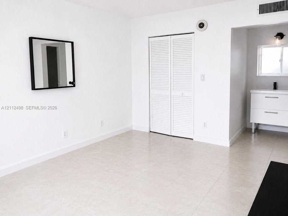 Neutral tile flooring, white louvered-door closet, modern white vanity with clean-lined hardware, and wall-mounted vanity lighting