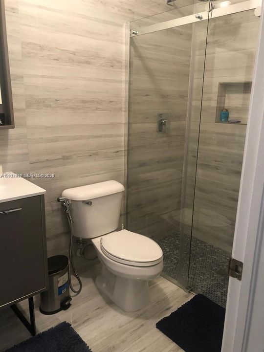 Bathroom featuring a glass-enclosed shower with pebble tile flooring, integrated wall niche, and wood-patterned wall tile with a matching vanity cabinet