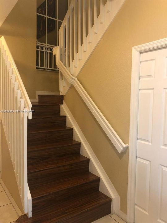 Staircase featuring wood-finish treads, white painted railings with balusters, and an integrated handrail