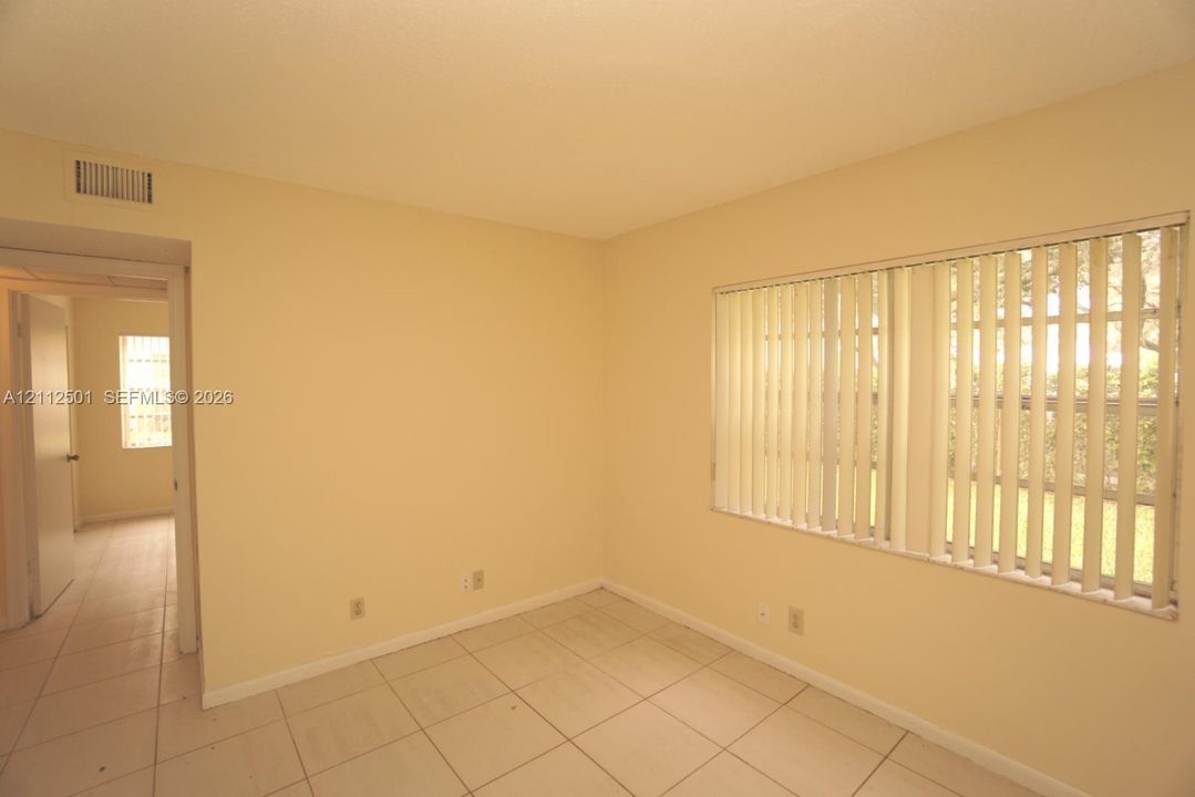 Interior space featuring light-toned tile flooring, neutral wall paint, and windows outfitted with vertical blinds