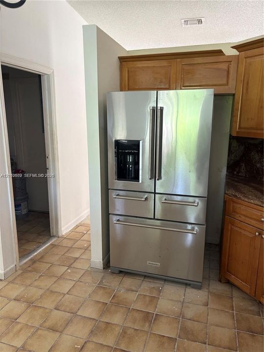 Kitchen featuring stainless steel multi-door refrigerator, natural wood-finish cabinetry, stone countertop, and ceramic tile flooring