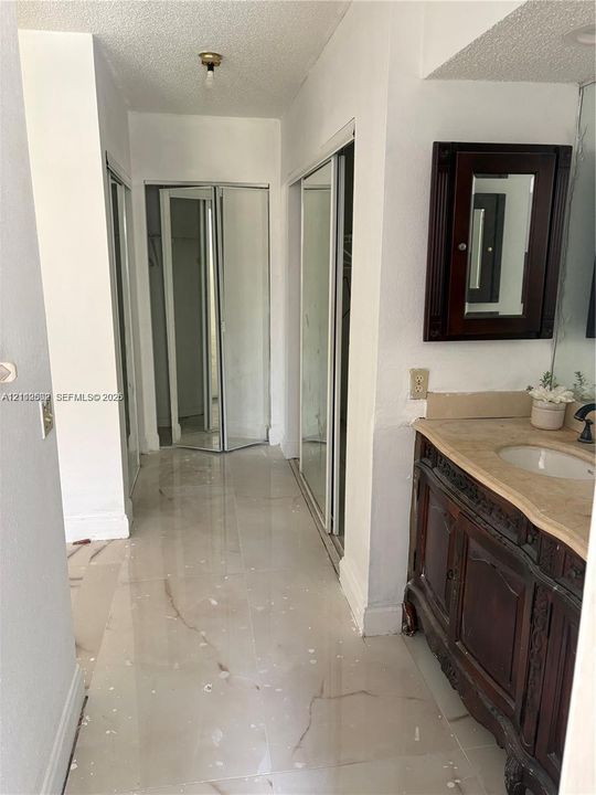 Bathroom featuring large-format tile flooring, a dark-stained wood vanity with a stone countertop, a wall-mounted mirrored medicine cabinet, and multiple mirrored closet doors