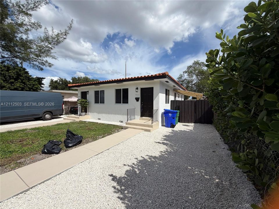 Exterior view featuring a white stucco facade, a low-pitched roof with clay tile trim, and a concrete walkway