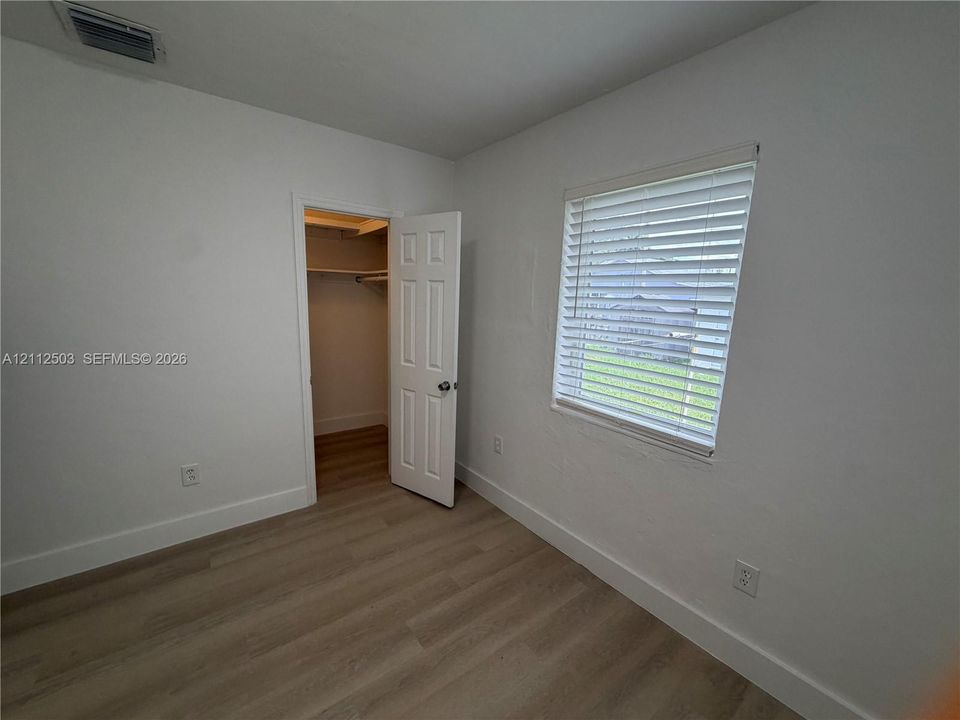 Interior room featuring light-toned wood-finish flooring, white walls, a closet with built-in shelving, and a window with horizontal blinds