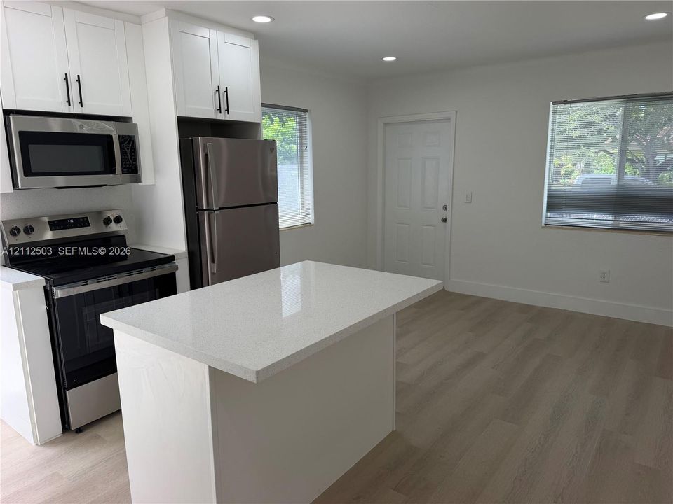 Kitchen featuring white shaker-style cabinetry, a central island with a quartz countertop, stainless steel appliances, and wood-finish flooring