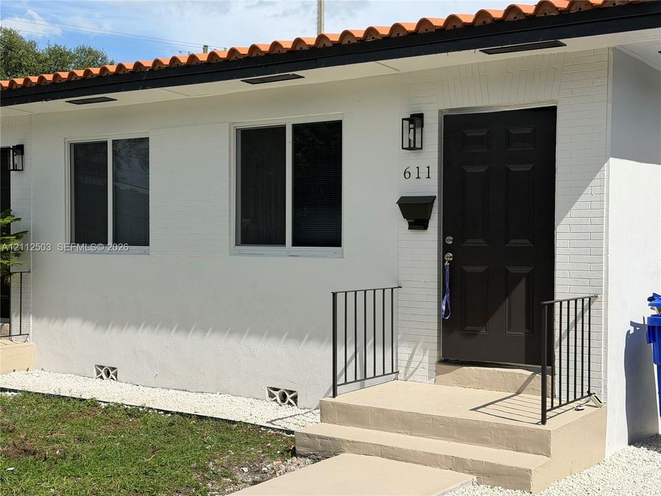 Exterior entrance featuring white painted brick, a mission-style barrel tile roofline, a solid panel front door, and black metal handrails