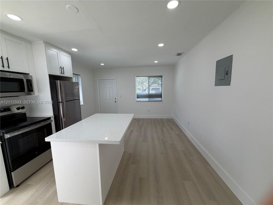 Kitchen featuring a central island with a solid surface countertop, white shaker-style cabinetry, stainless steel appliances, and wood-finish flooring