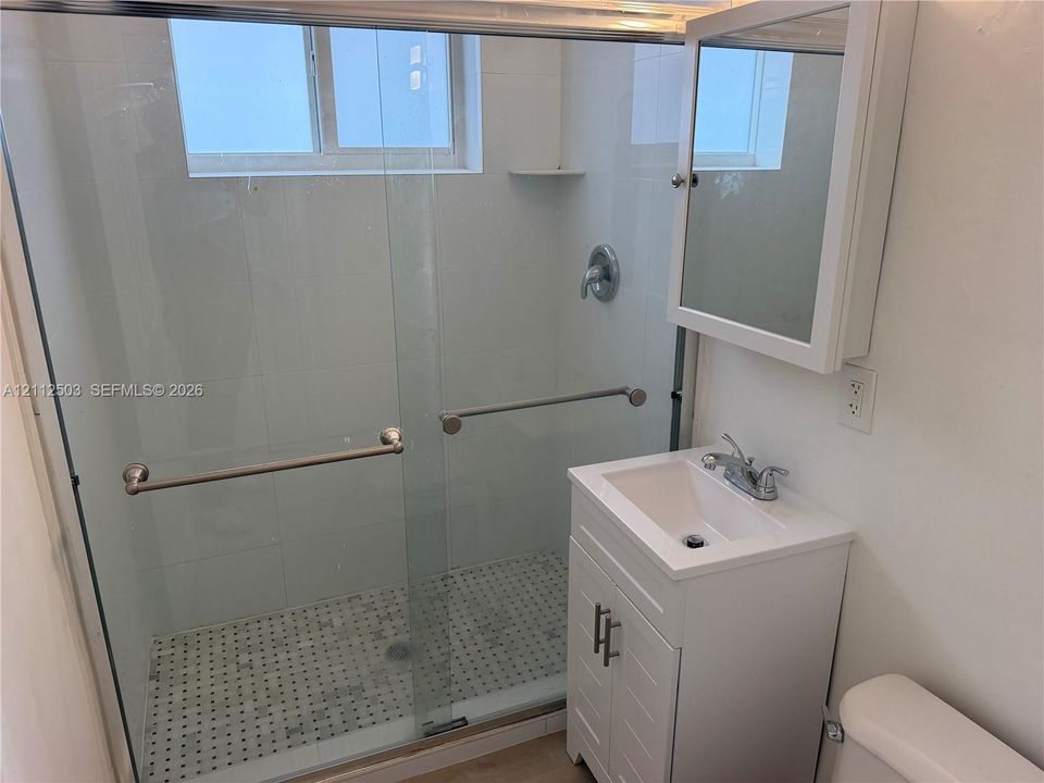Walk-in shower with a glass enclosure, mosaic tile floor, vanity cabinet with a integrated sink, and a wall-mounted mirrored medicine cabinet