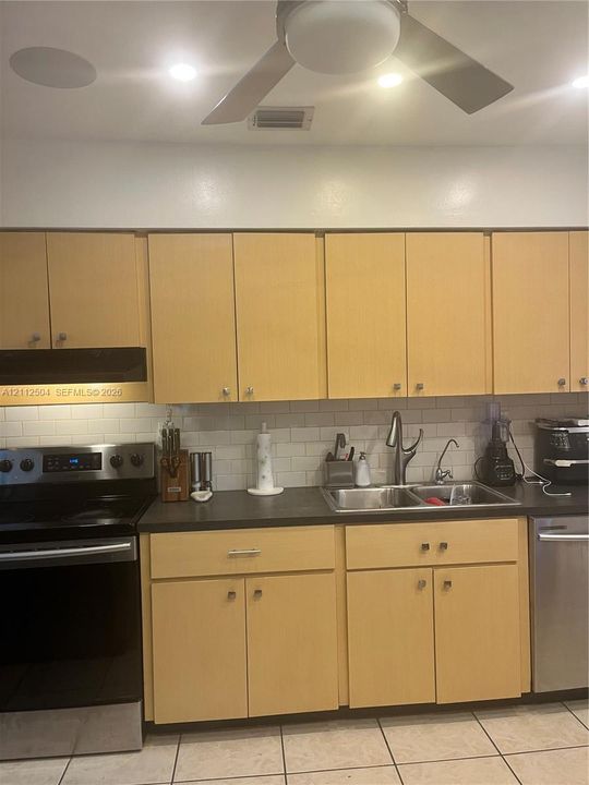 Light wood cabinetry, subway tile backsplash, stainless steel appliances, dark countertops, and ceiling-mounted light fixture