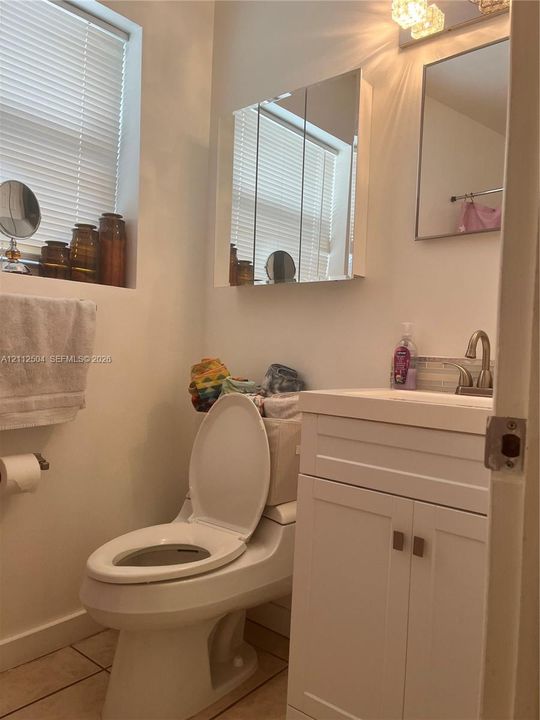 White vanity cabinet with an integrated sink and metal faucet, tri-fold mirrored medicine cabinet, and ceramic tile flooring
