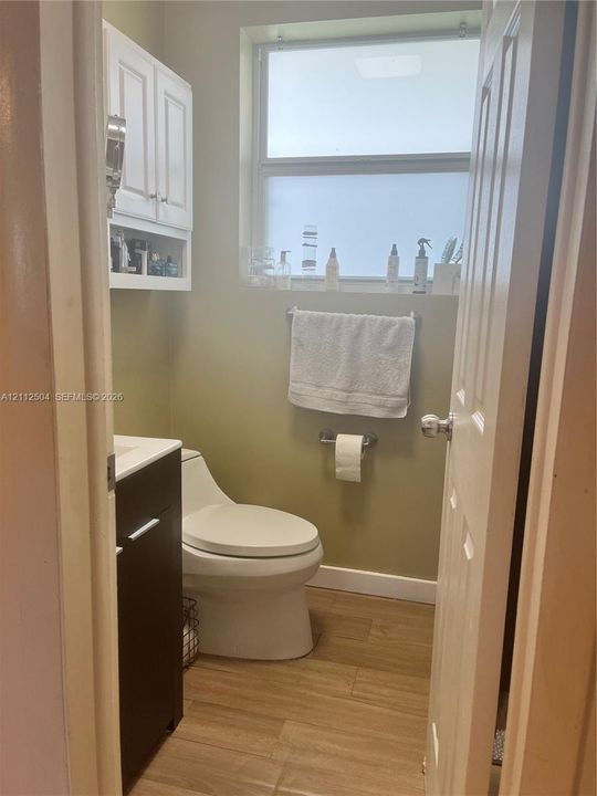 Restroom featuring wood-finish flooring, a contemporary dark-finish vanity, a white high-profile toilet, white built-in wall cabinetry, and an opaque glass window
