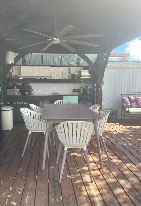 Covered outdoor pavilion featuring wood-finish decking, dark-toned cabinetry, built-in shelving, and a ceiling-mounted fan