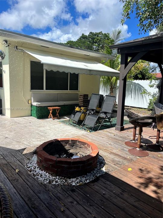 Outdoor patio featuring a circular brick fire pit with stone fill, a retractable wall-mounted awning, and a wooden deck