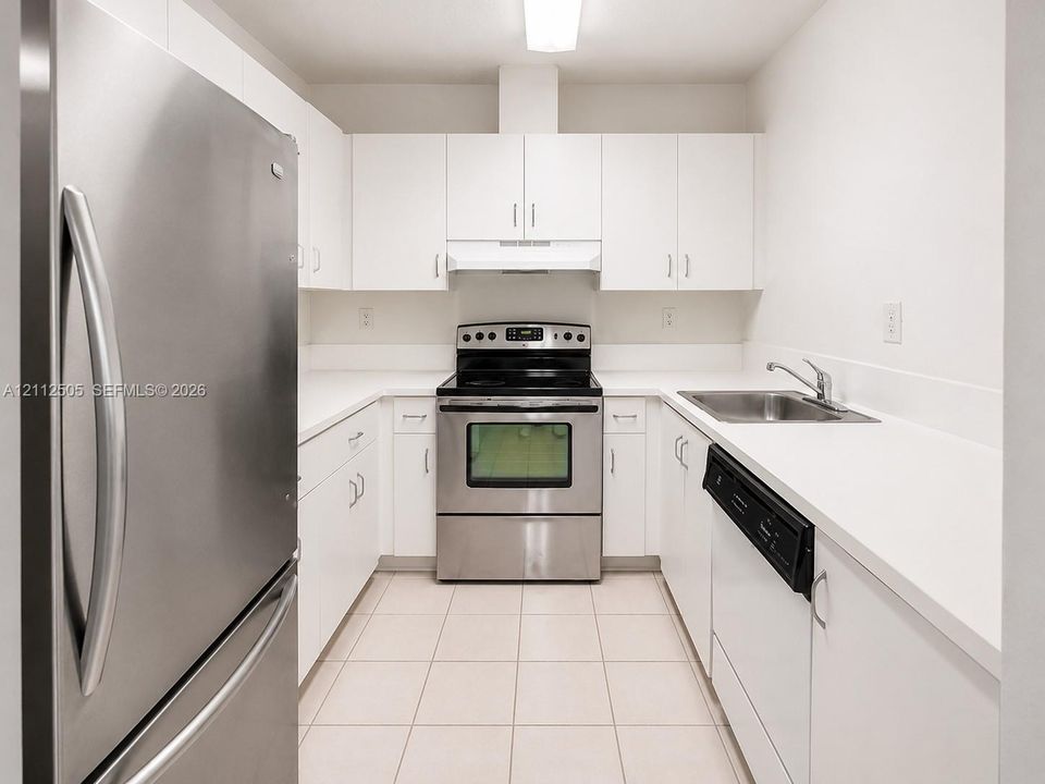 Kitchen featuring white cabinetry, stainless steel appliances, solid surface countertops, a stainless steel sink with a deck-mounted faucet, and ceramic tile flooring