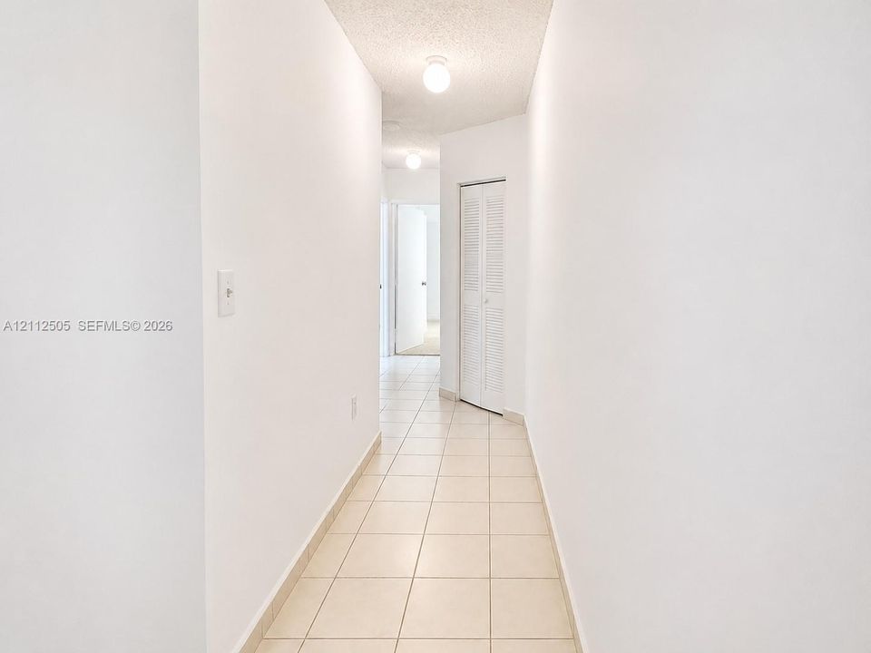 Hallway featuring neutral-toned tile flooring, white walls, and a bi-fold louvered closet door with flush-mount ceiling lighting