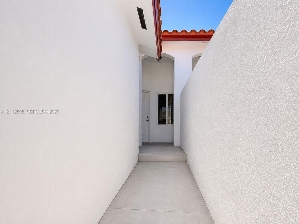 Exterior passageway featuring smooth white stucco walls, a concrete walkway, elevated threshold, and terra-cotta tile roofline
