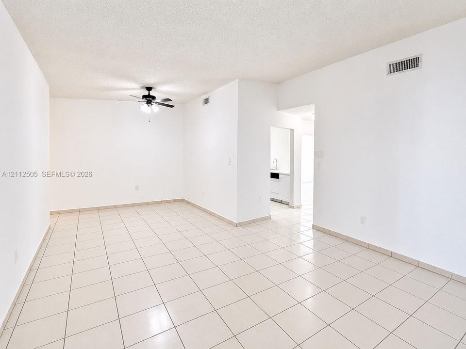Open interior space featuring neutral ceramic tile flooring, bright white wall finishes, and a ceiling-mounted fan with integrated light fixture