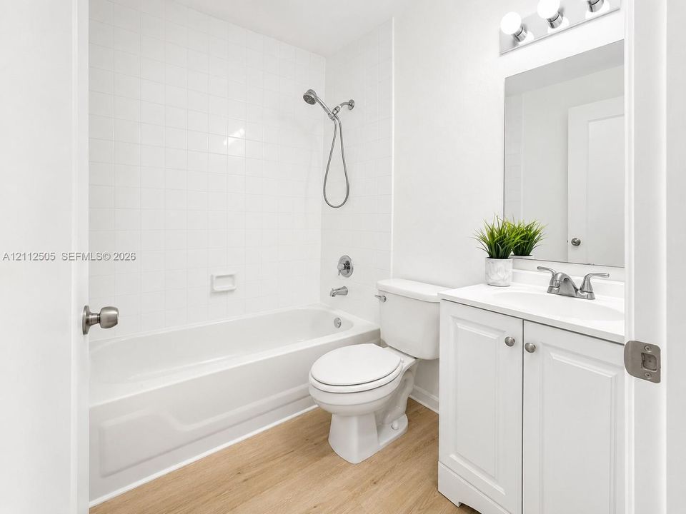 Full bathroom featuring a tub-shower combination with white wall tile, white vanity cabinet with integrated sink, wood-finish flooring, and vanity light fixture