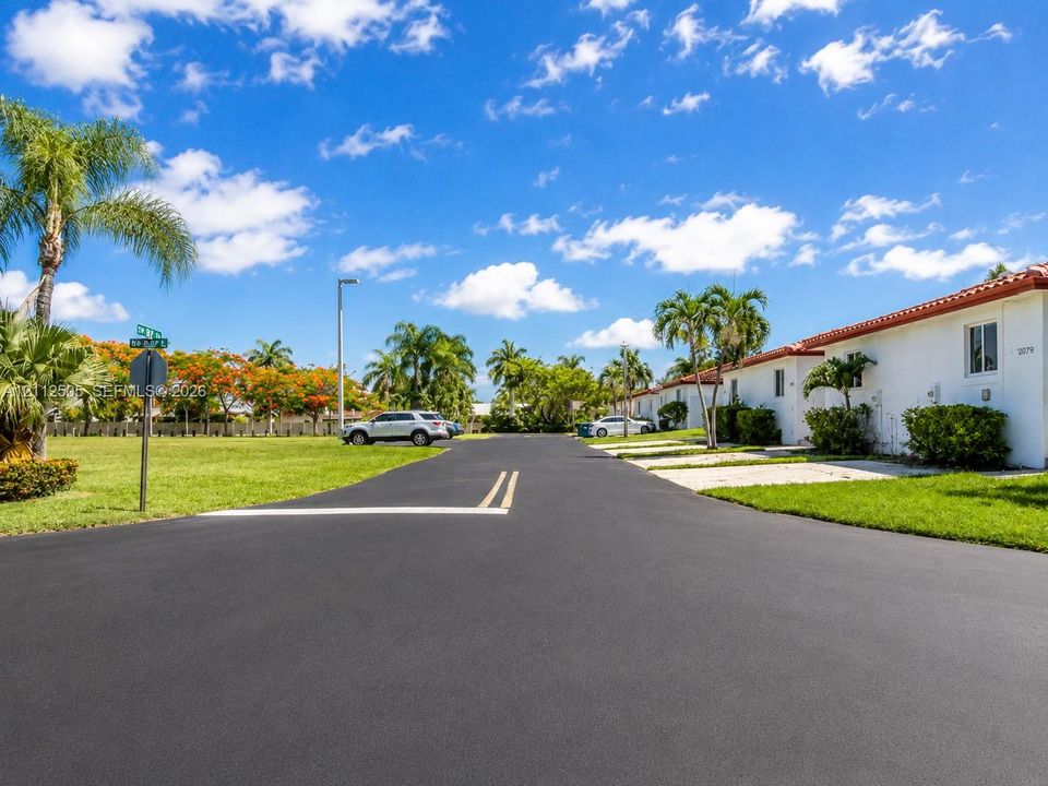 White stucco exterior featuring a red tile roof, paved driveway, and mature palm tree landscaping
