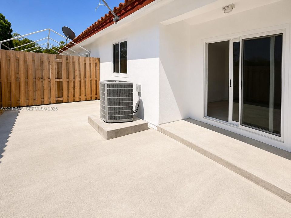Concrete patio featuring a sliding glass door entry, white exterior stucco walls, wood-slat privacy fencing, and tile roof detailing