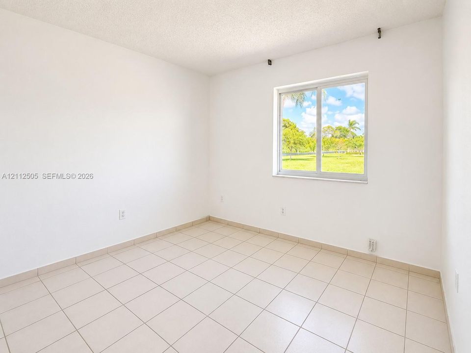 Neutral-toned ceramic tile flooring, crisp white walls, and a single-pane sliding window providing exterior green space exposure