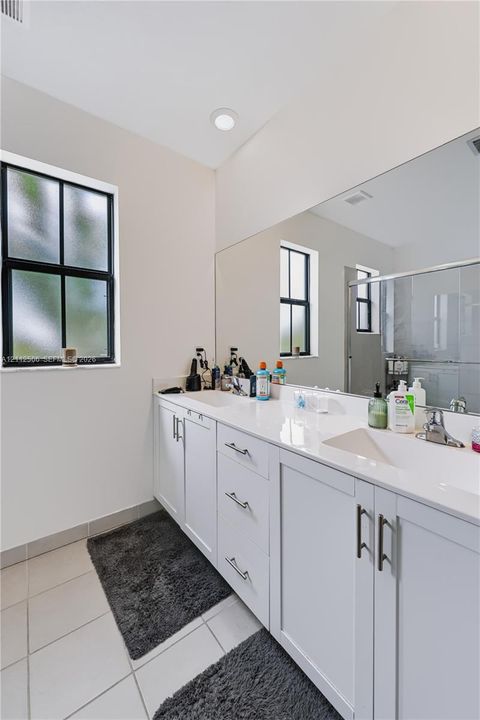 Dual-sink vanity featuring white shaker-style cabinetry, solid-surface countertop, integrated rectangular sinks, and large wall-mounted mirror