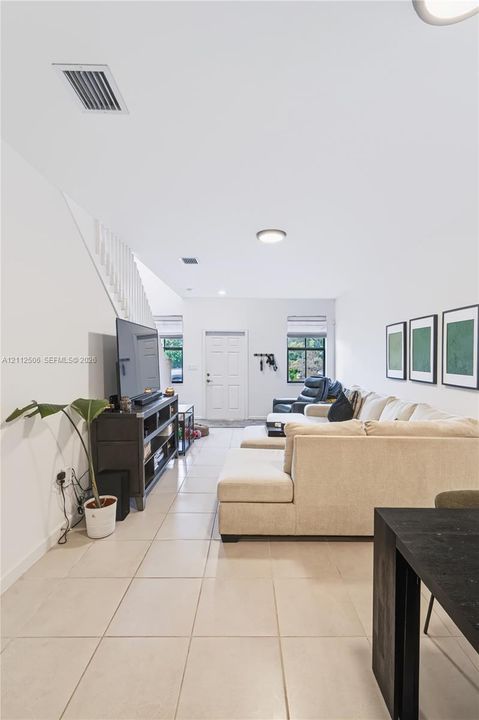 Open-concept interior featuring neutral ceramic tile flooring, a white staircase with a vertical balustrade, and dual windows