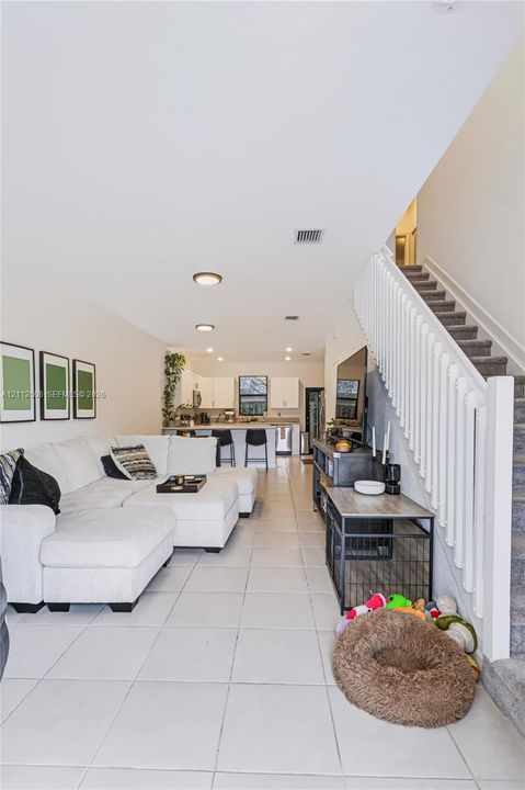 Open-concept floor plan featuring tile flooring, white cabinetry, a kitchen island, and a staircase with white balusters