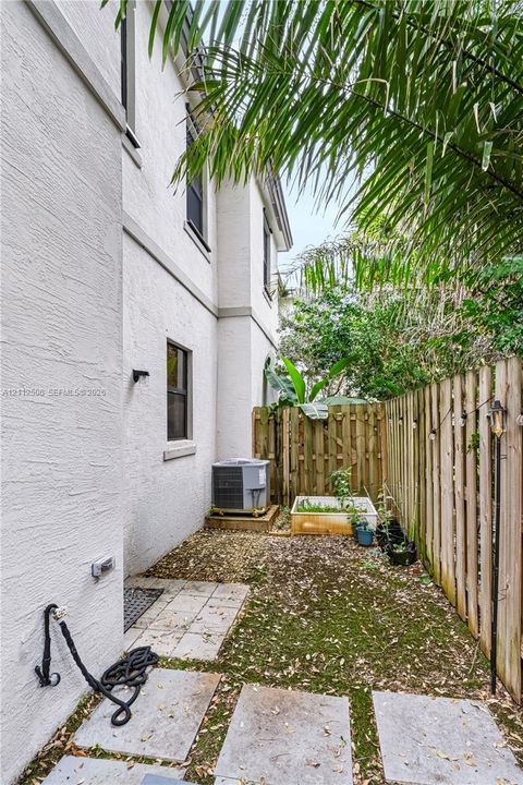 Stucco exterior side yard featuring concrete paver stones, a wooden privacy fence, and native landscaping
