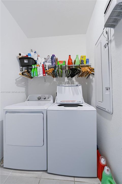 Dedicated laundry area featuring tile flooring, wall-mounted wire shelving, and a white breaker panel