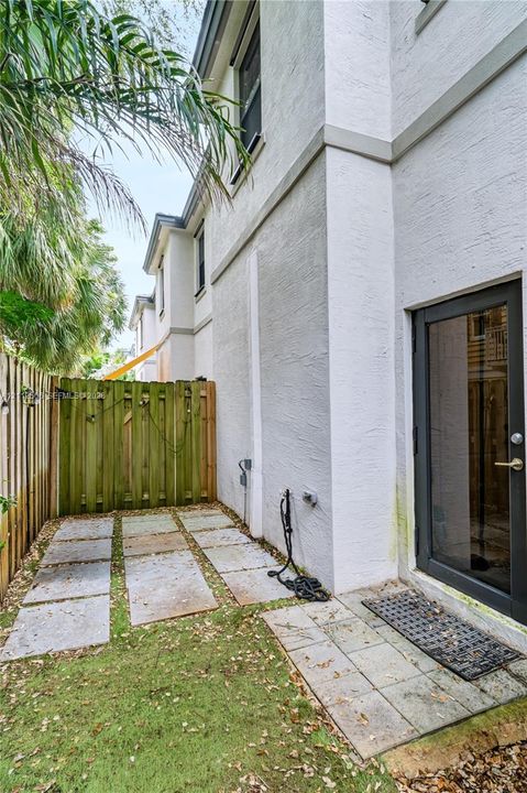Exterior side yard featuring stucco siding, stone paver pathway, and enclosed wood fencing