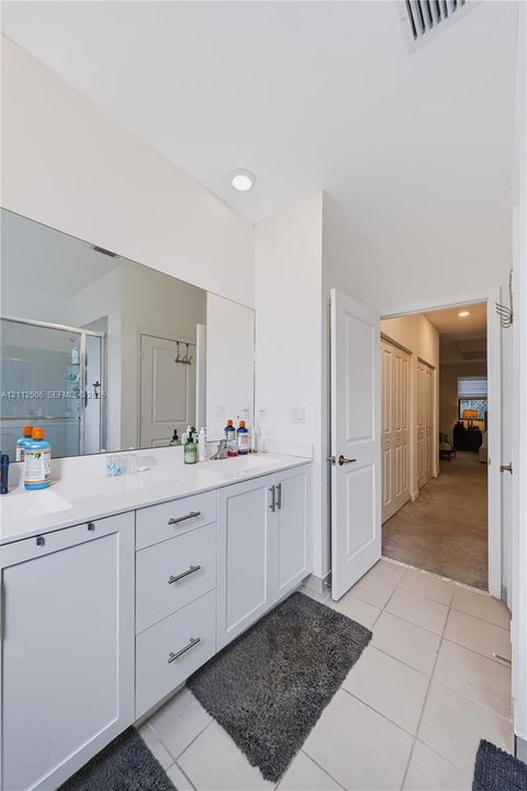 Bathroom featuring a dual-sink vanity with white cabinetry, solid-surface countertops, polished chrome fixtures, and a large-format vanity mirror
