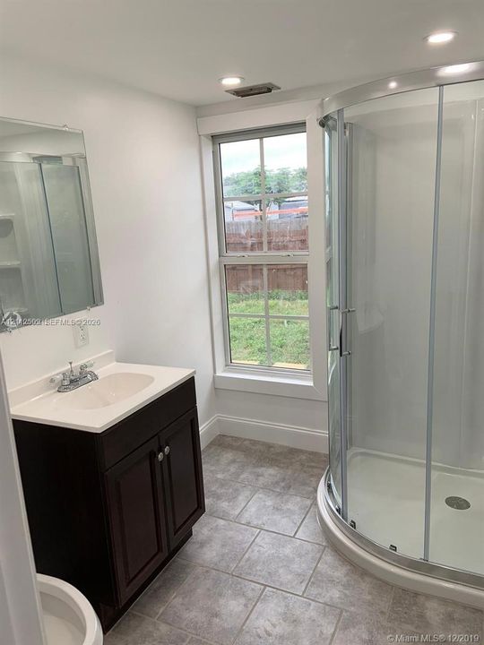 Bathroom featuring a dark wood-finish vanity, light-toned countertop with an integrated sink, curved glass-enclosed shower, and tile flooring