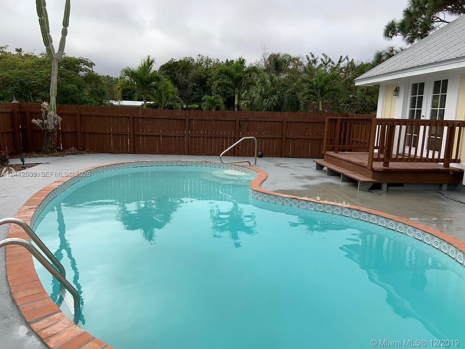 Curved in-ground pool with decorative tile border and brick coping, elevated wood deck, and perimeter wood privacy fencing