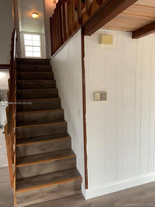 Staircase with wood-finish treads, vertical paneling, and a natural wood-finish railing