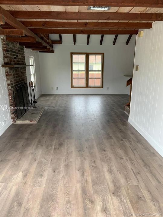 Exposed wood ceiling beams, floor-to-ceiling brick fireplace with a stone hearth, and wood-finish flooring