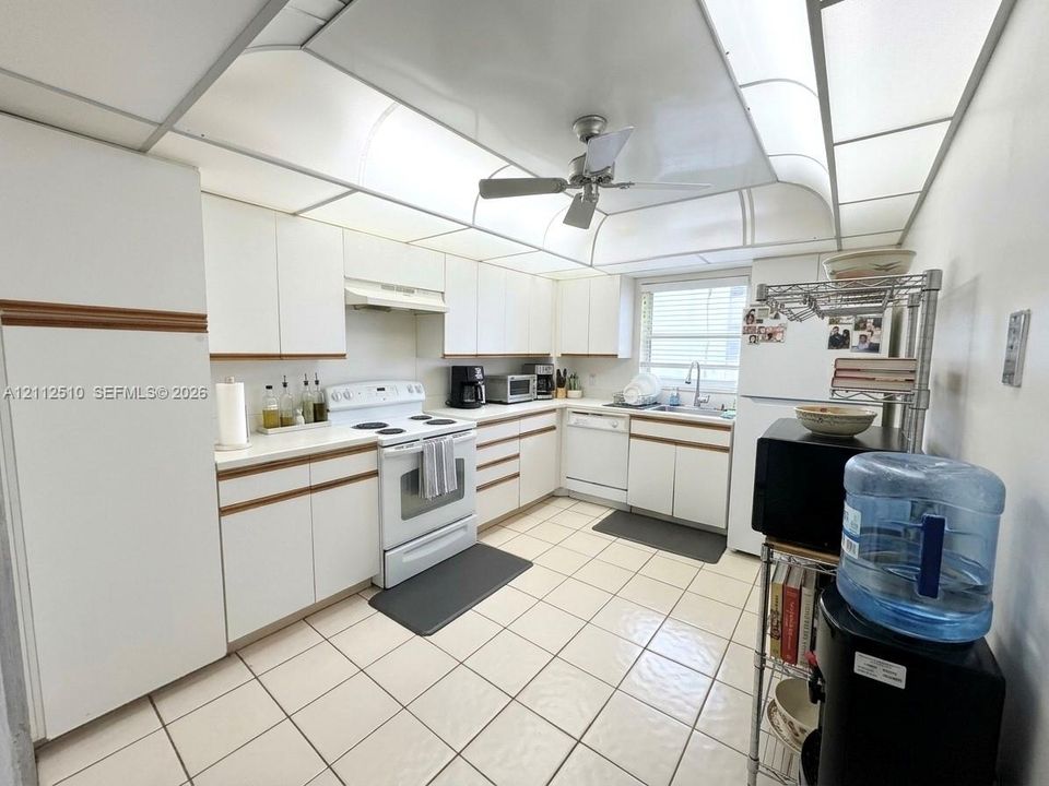Kitchen featuring white flat-panel cabinetry, light-toned tile flooring, integrated ceiling lighting, and a white appliance suite including a range and dishwasher