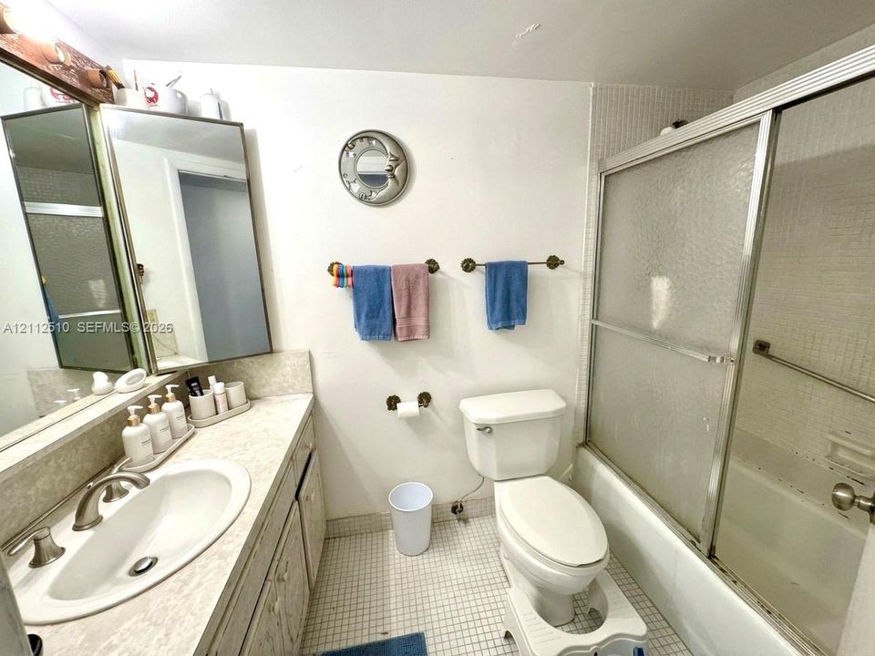 Bathroom featuring a vanity with an integrated oval sink, countertop, tri-panel mirrored cabinet, mosaic tile flooring, and a tub-shower combination with sliding glass doors
